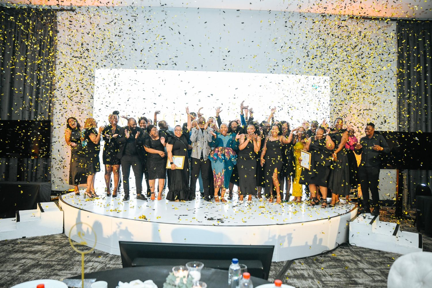Award winners celebrating on stage under falling gold and black confetti