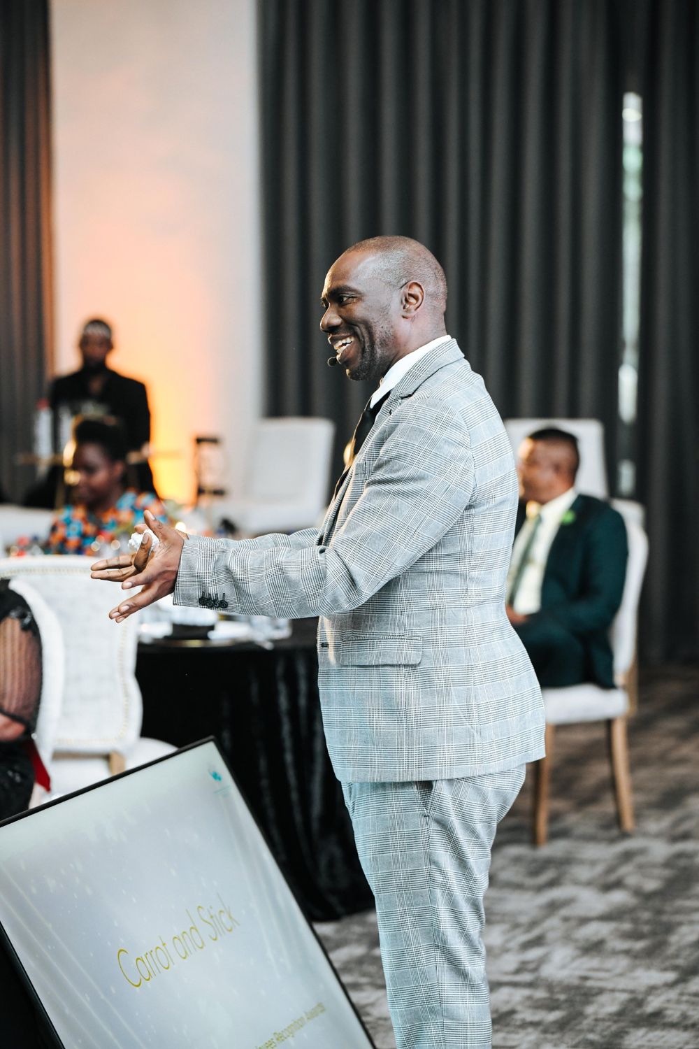 Speaker in a grey check suit addressing the room