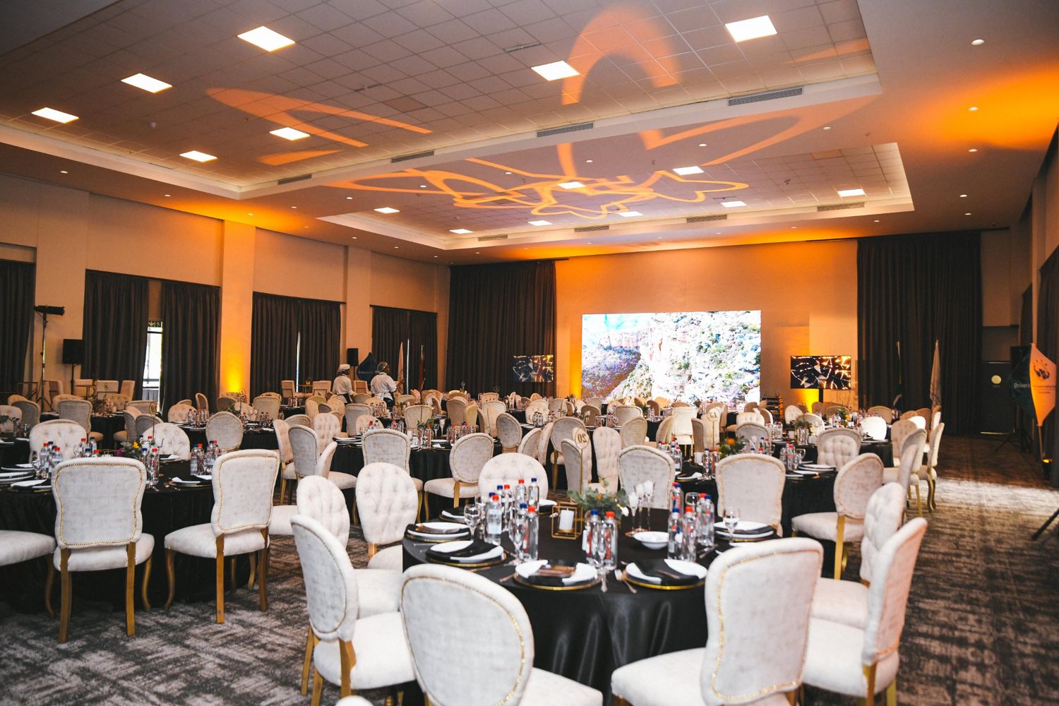 Banquet hall with white and gold chairs, black tables and amber gobo lighting
