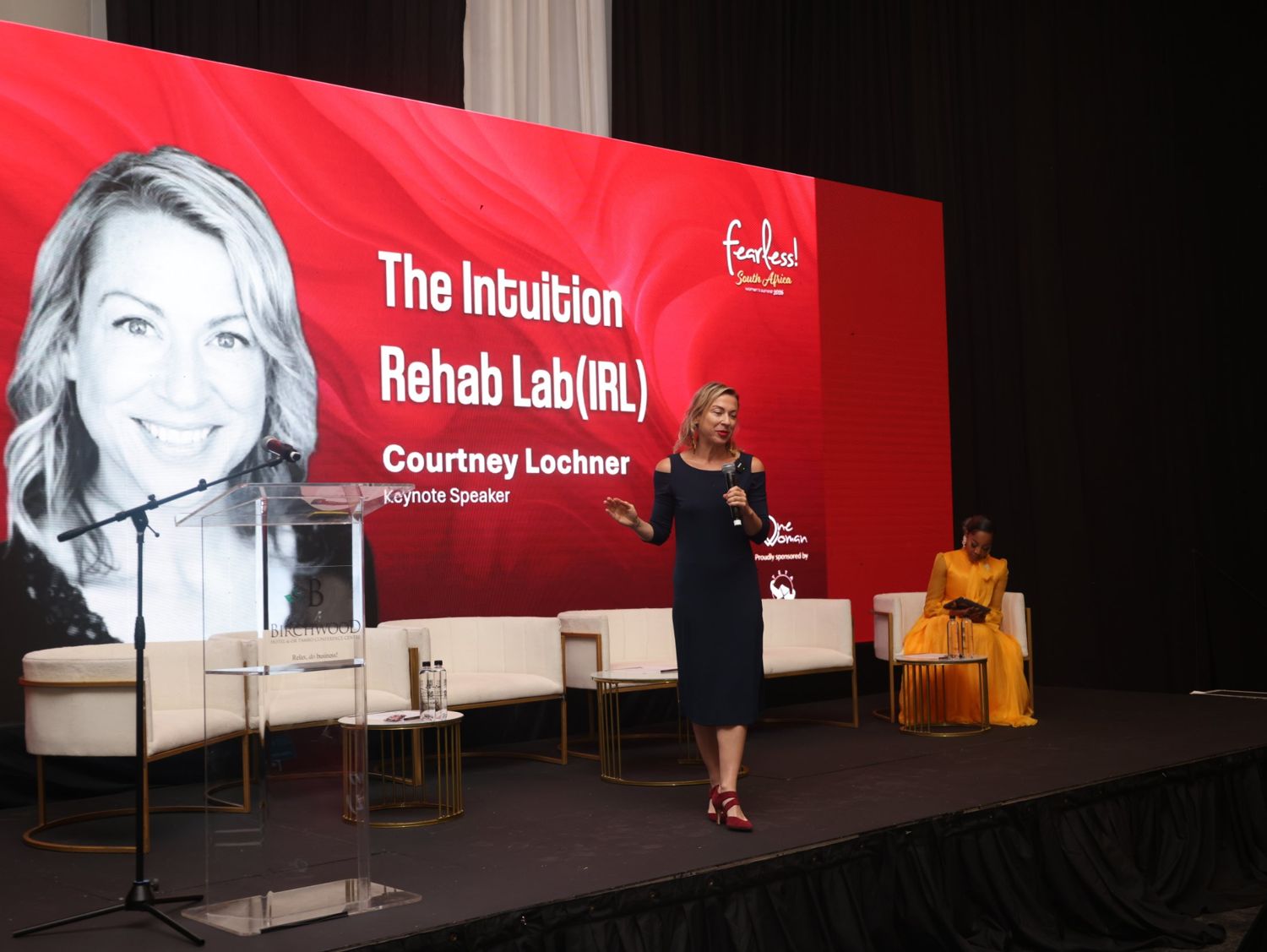 Courtney Lochner speaking on stage in front of her keynote title graphic