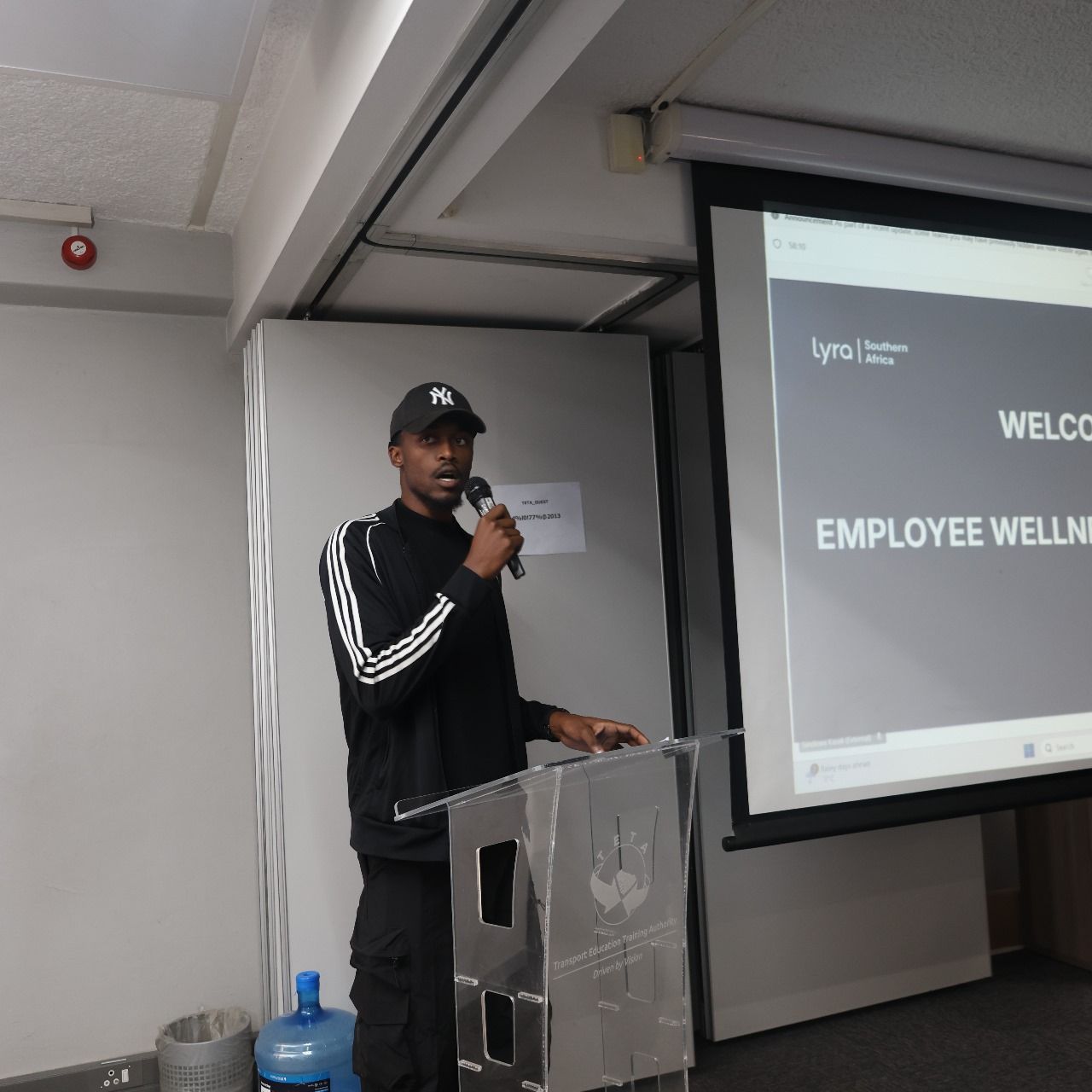 Speaker at a perspex podium beside an Employee Wellness welcome slide